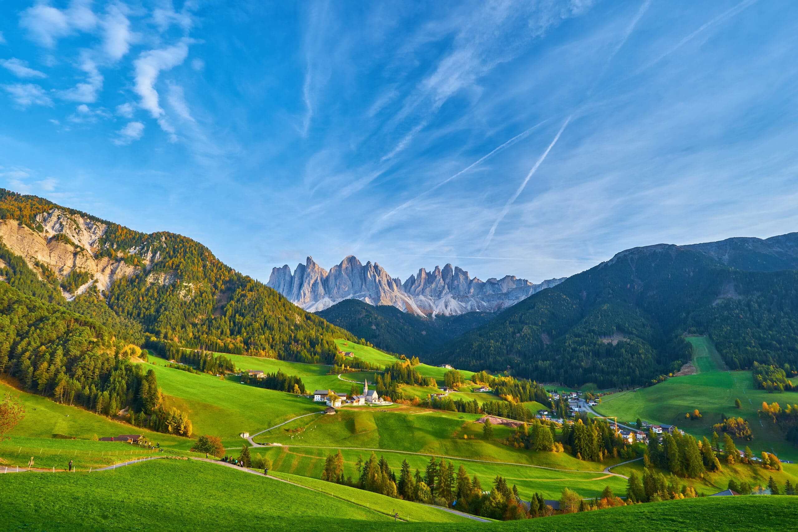 Amazing autumn scenery in Santa Maddalena village with church, colorful trees and meadows under rising sun rays. Dolomite Alps, South Tyrol, Italy.